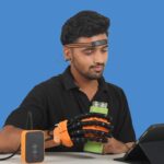 Exploded diagram of Rehabveda R1 system showing EEG headband, AI unit, and pneumatic glove